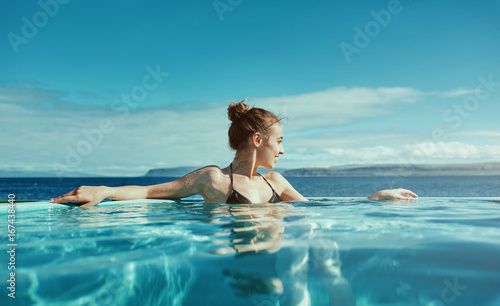 Young cheerful girl swimming in water of pool looking away on background of sea, Iceland, West Fjords. 