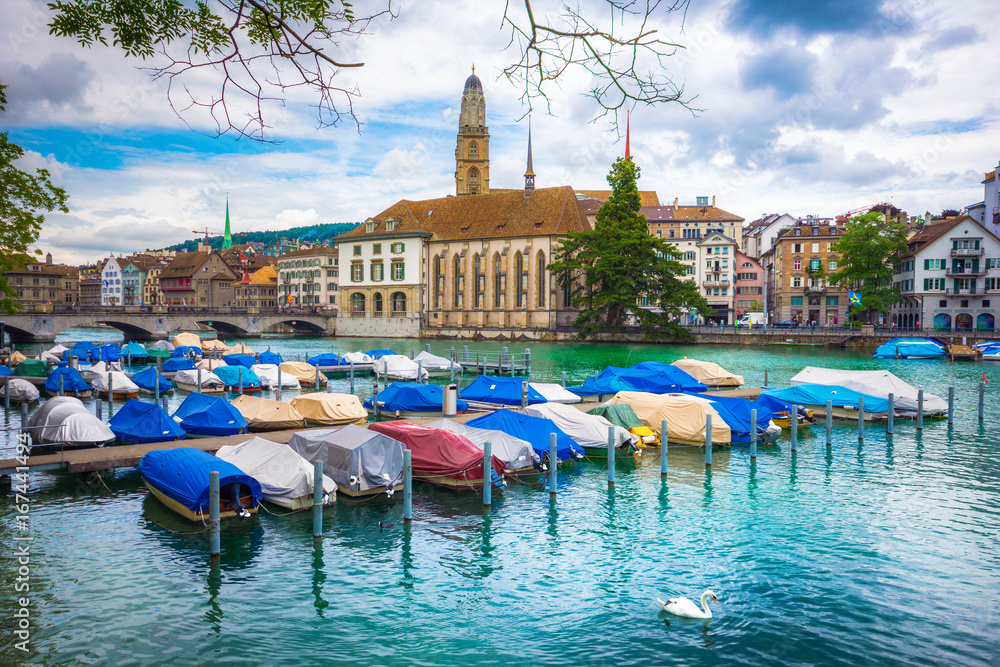 Beautiful view of historic city center of Zurich with famous Fraumunster Church and Munsterbucke crossing river Limmat with anchored boats on a cloudy day, Canton of Zurich, Switzerland