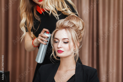Closeup view of a hairdresser coiffeur makes evening hairstyle to the blond model in salon