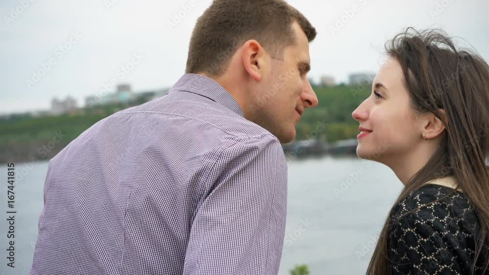 Kiss of young couple at the river at sunset. Guy and woman are spending time on date Kiss of young couple at the river at sunset. Guy and woman are spending time on date