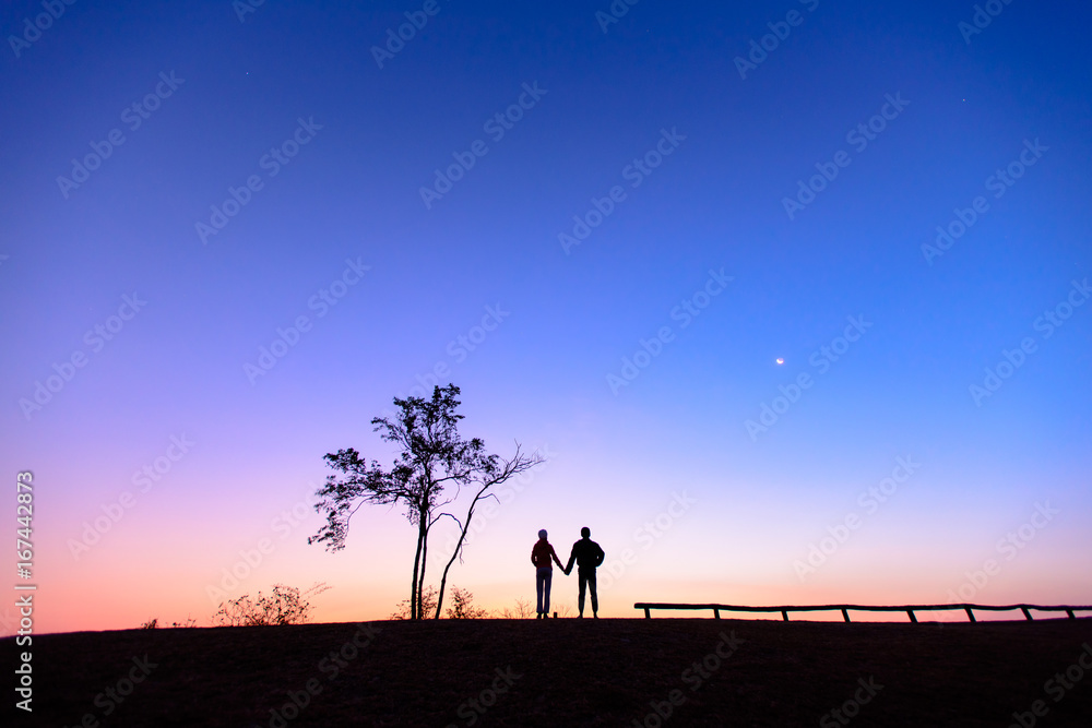 Silhouette of a lovely couple watching beautiful sunrise on the mountain.  Dawn light and beautiful sky with copy space. Romantic love of couple concept.
