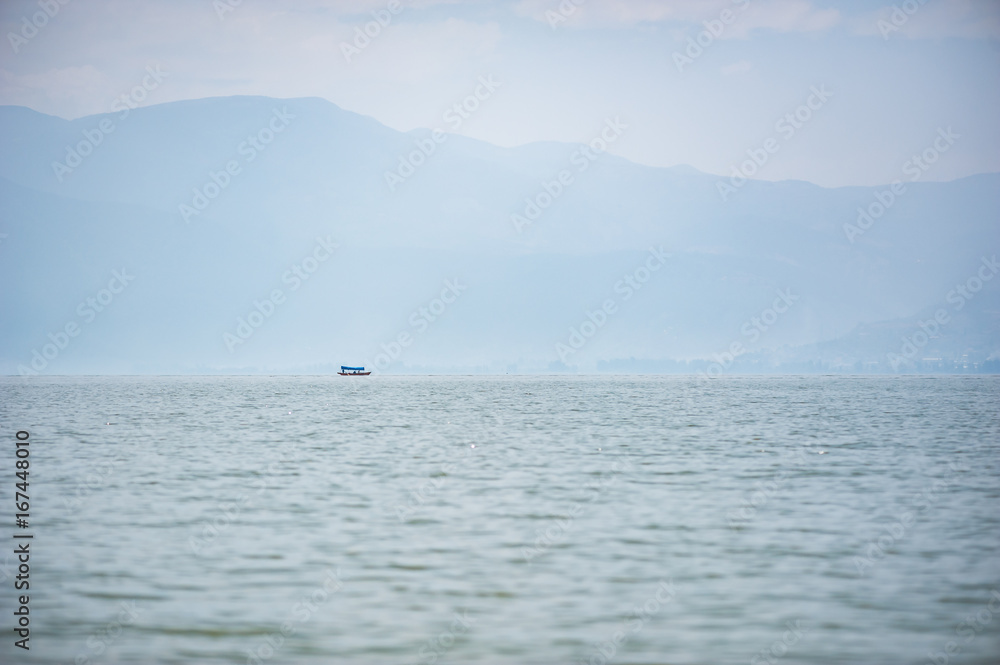 Small boat on a lake in the haze with mountains in the background, Xichang, China