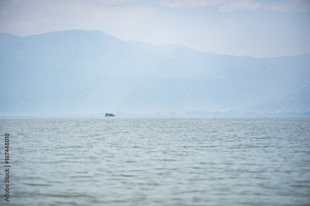 Small boat on a lake in the haze with mountains in the background, Xichang, China Small boat on a lake in the haze with mountains in the background, Xichang, China