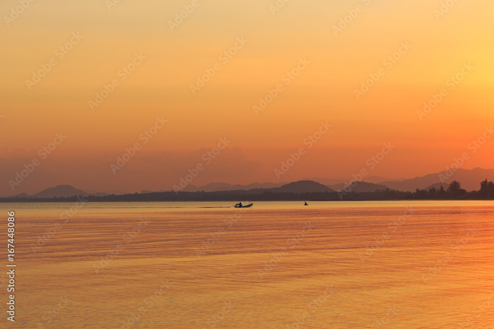 Sunset on the sea water, small boat on the water, horizon line and hills on background, Thailand