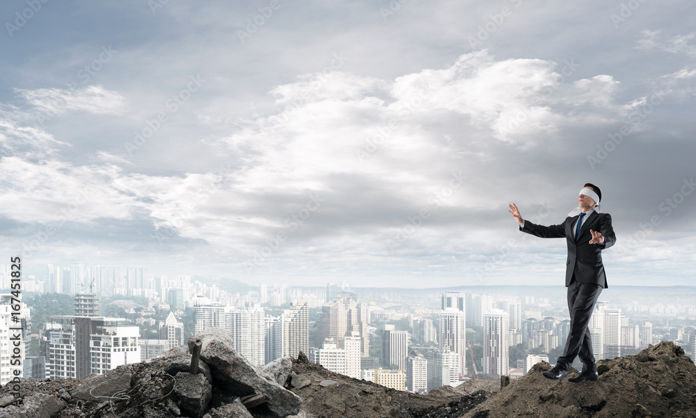 Young businessman in blindfold walking carefully and cityscape at background Young businessman in blindfold walking carefully and cityscape at background