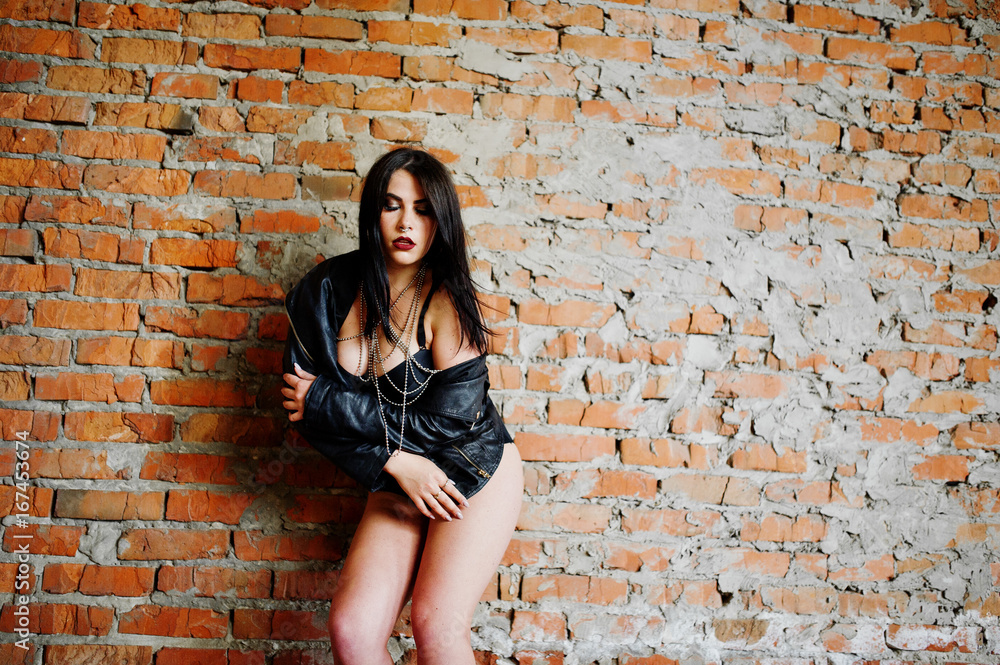 Brunette plus size sexy woman, wear at black leather jacket, lace panties, bra at abadoned place near brick wall.