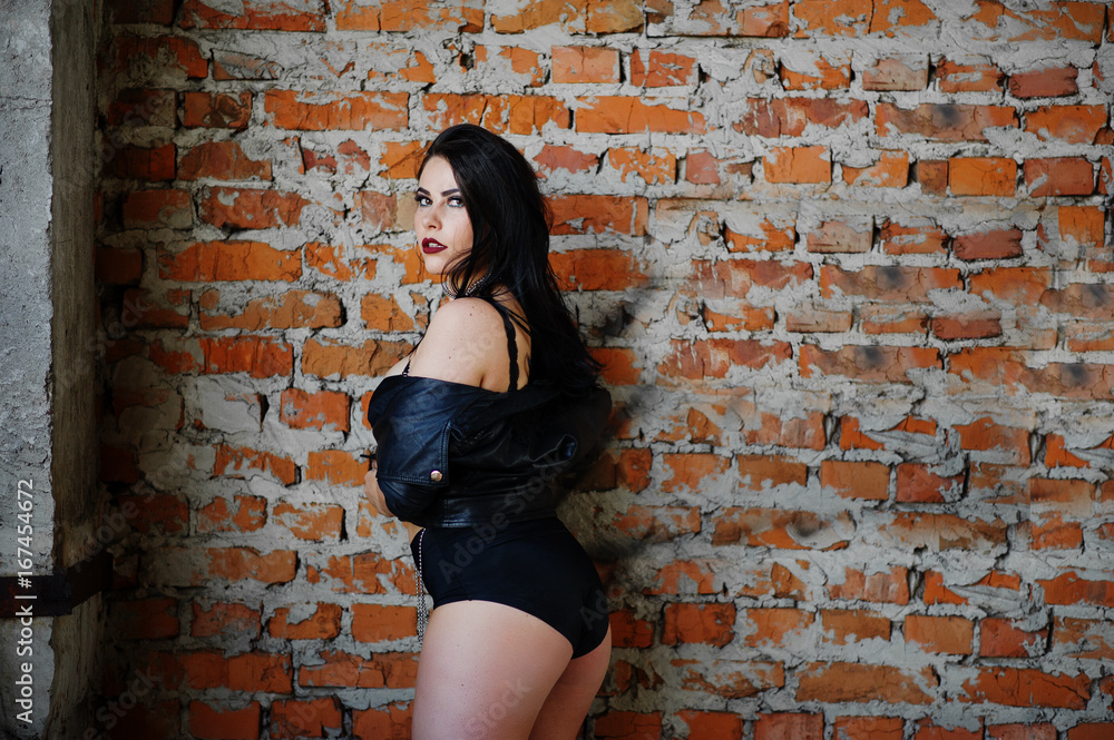 Brunette plus size sexy woman, wear at black leather jacket, lace panties, bra near brick wall at abadoned place.