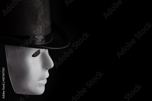 White mask profile wearing black top hat isolated on black background with copy space
