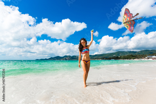 Sexy girl in a bright swimsuit launches a kite on the seashore, a tropical island, summer vacation, a woman runs the mountains in the background