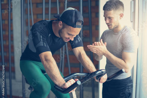 Young man exercise on stationary bikes in fitness class. Man workout in gym. Exercise on elliptical machine. Man personal trainer.