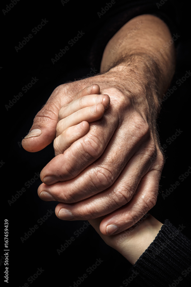 Fototapeta premium Hands of an elderly man holding the hand of a younger man.