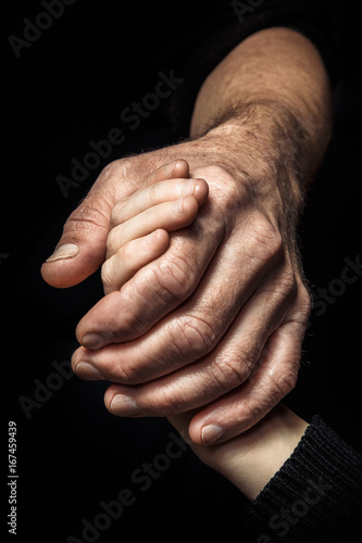 Hands of an elderly man holding the hand of a younger man.
