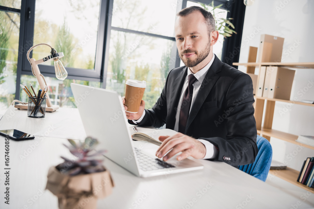 handsome young businessman using laptop with cup of coffee handsome young businessman using laptop with cup of coffee