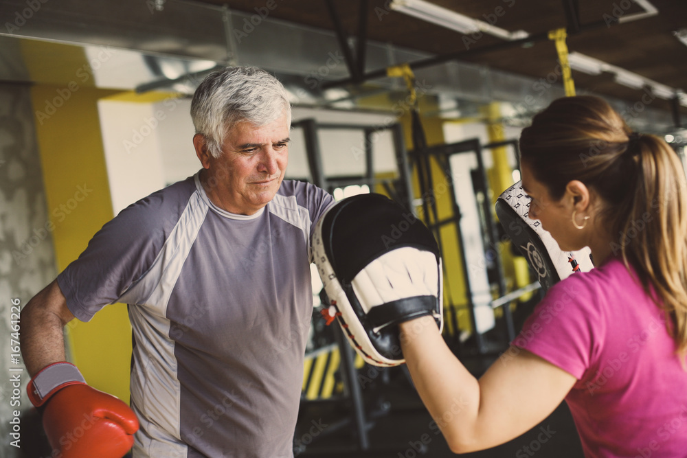 Older man boxing in gym. Senior man with personal trainer.