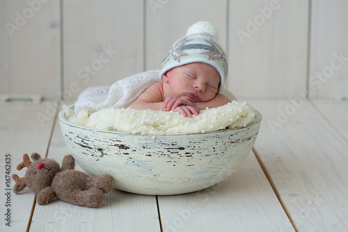 The newborn boy lies in a round bowl on a white plaid and sleeps sweetly with his hands under his head