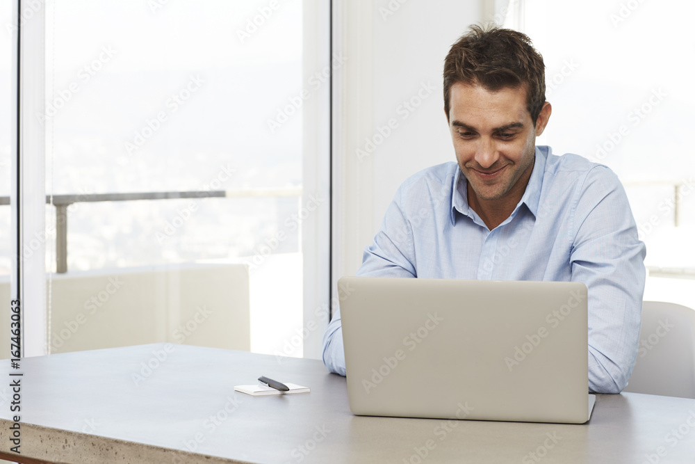 Man at home using laptop on desk, smiling Man at home using laptop on desk, smiling