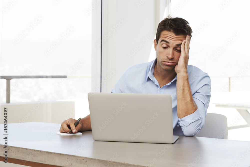 Bored man using laptop on desk at home Bored man using laptop on desk at home
