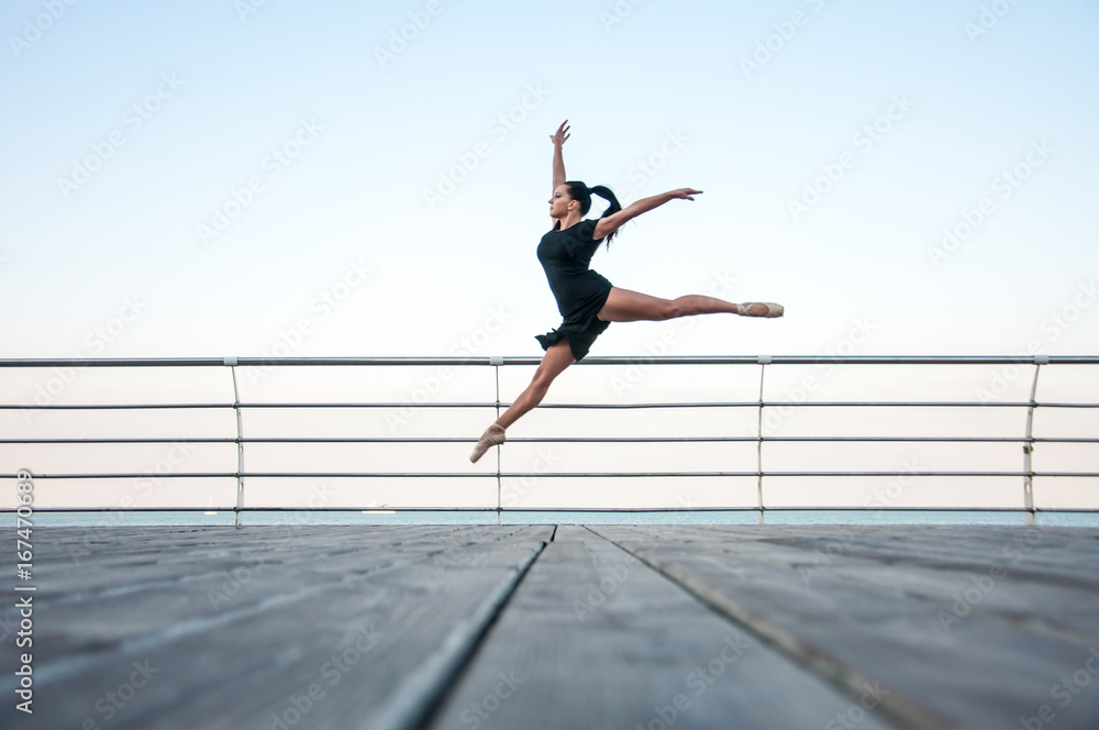 Young beautiful gymnast doing gymnastic jumps outdoors near the sea