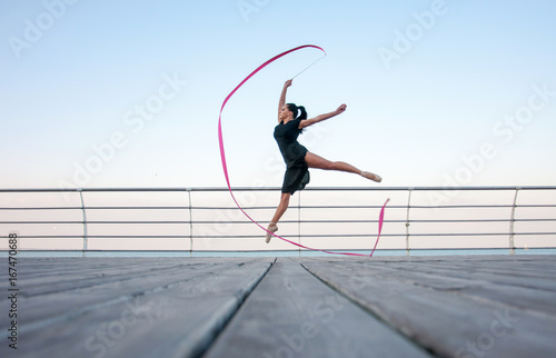 Young beautiful ballerina doing gymnastic jumps outdoors near the sea