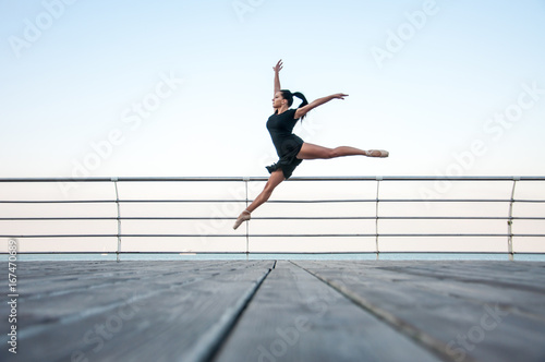 Young beautiful gymnast doing gymnastic jumps outdoors near the sea