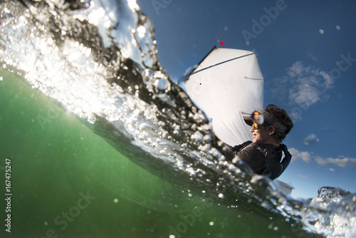 Over under close up image of a boy sailing an optimist class dinghy