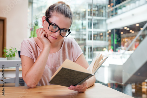 Relaxed smiling girl reading book in cafe at shopping mall