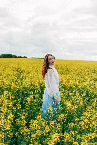 Beautiful girl in a dress among yellow flowers in a field © Денис Кипкаев