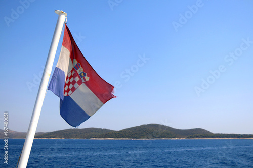 Croatian flag on a boat, blowing in the wind. Beautiful coast in the background. Selective focus. 