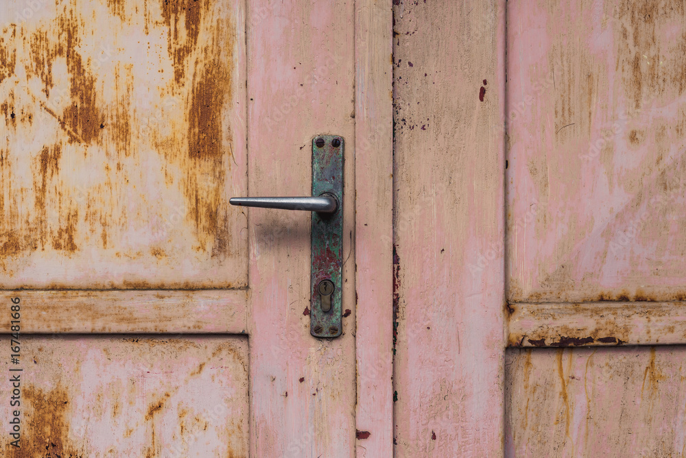 closeup at rusty pink garage door or gate and its handle, old and desolate, damaged paint, scratches