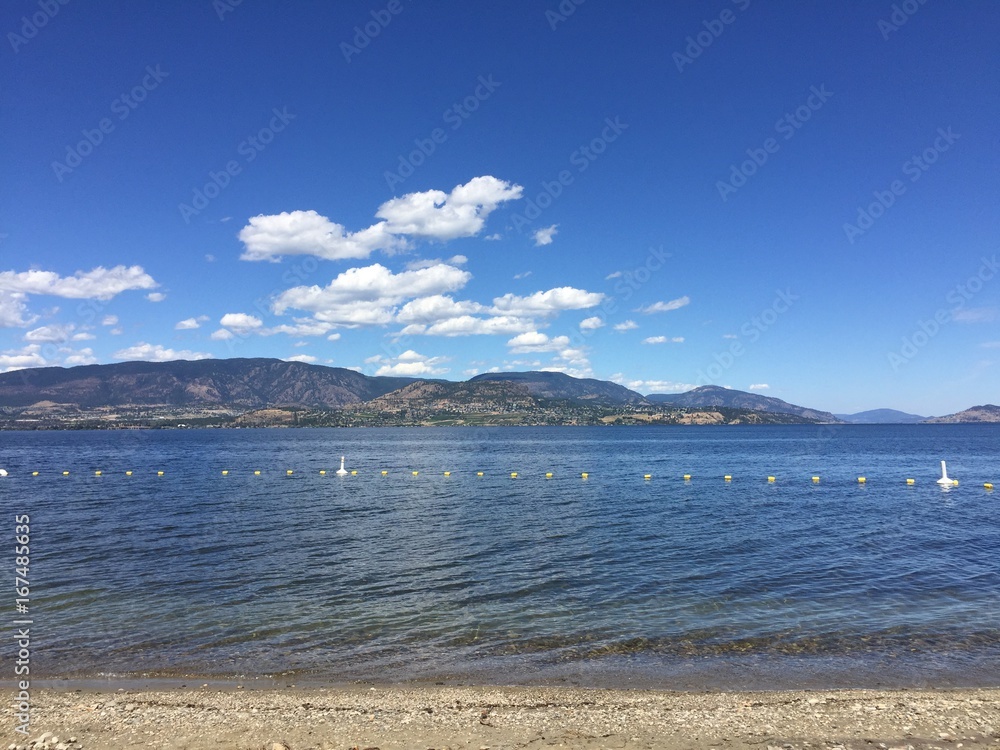 Scenic summer lake and mountains landscape view with sandy beach.
