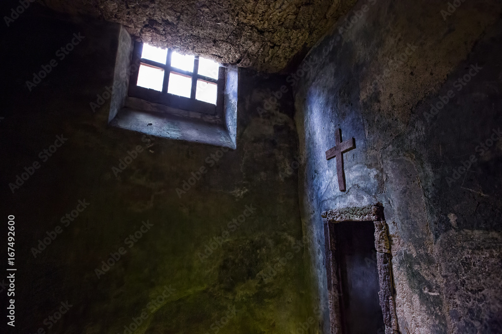 Catholic cross and light from the window in the stone room of the old monastery