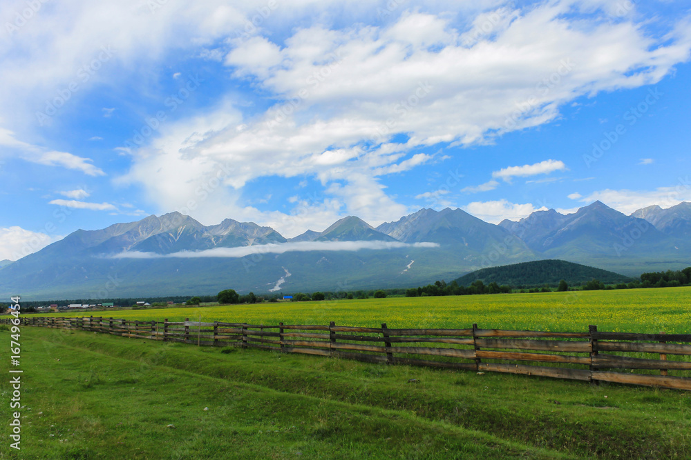 Obraz premium wooden fence and a green glade against the backdrop of the mountains