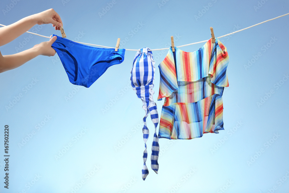 Female hands hanging out beachwear on a line. Summer vacation concept - obrazy, fototapety, plakaty 