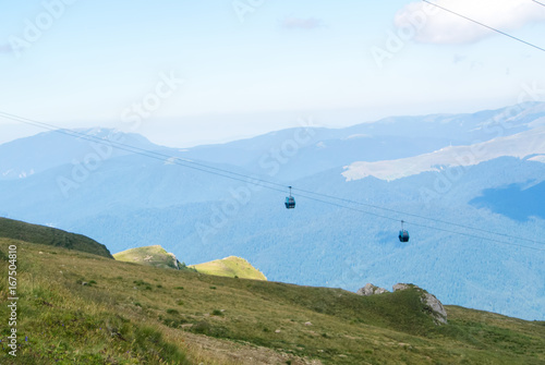 Panoramic view over the Carpatian mountains and two cableway cabins moving to the top of the mountain at the background, Bucegi natural park near Sinaia, Romania, on sunny summer day.