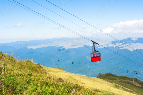 A view to red open cableway cabin over the top of the mountain and beautiful landscapes with blue mountains, green walley, Bucegi natural park, Sinaia, Romania.