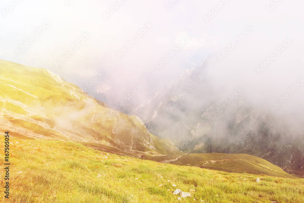 Φωτογραφία Toned panoramic view over the Carpatian mountains, serpentine path and a big fog cloud at the background, Bucegi natural park, Romania, on sunny summer day