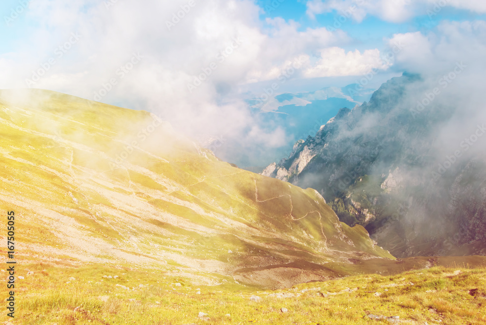 Φωτογραφία Toned panoramic view over the Carpatian mountains, serpentine path and a big fog cloud at the background, Bucegi natural park, Romania, on sunny summer day