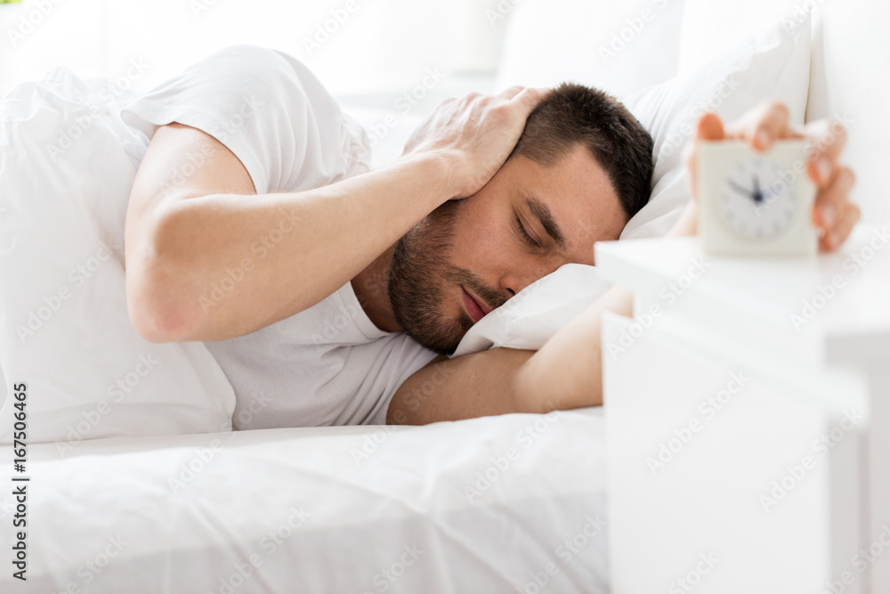young man in bed reaching for alarm clock young man in bed reaching for alarm clock