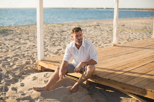 The man in the white shirt and shorts sitting on the beach.