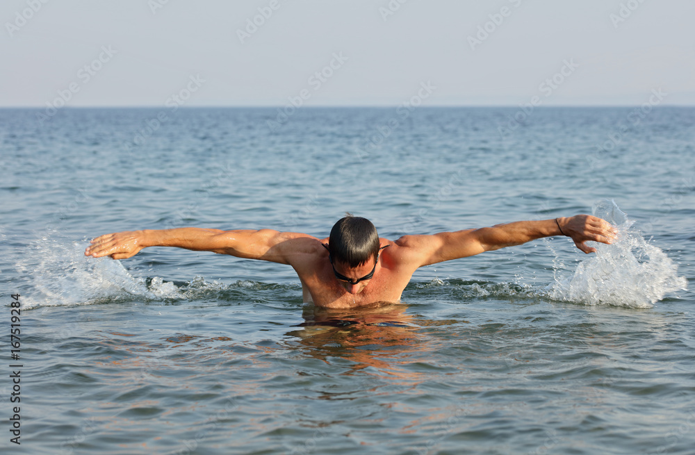 Strong muscular man swimming i butterfly style. Active summer holiday vacation. Sport, healthy lifestyle concept