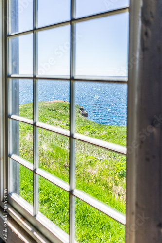 Looking through old window of house with cliff and ocean view in Bonaventure Island  Quebec  Canada
