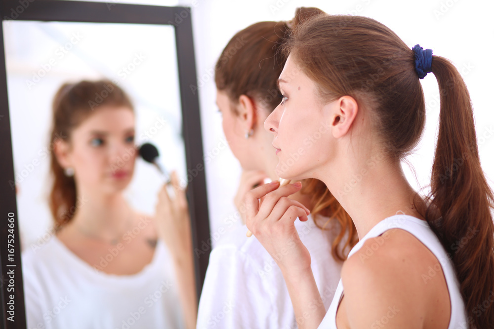 Beautiful girls looking in the mirror and applying cosmetic with a big brush Beautiful girls looking in the mirror and applying cosmetic with a big brush