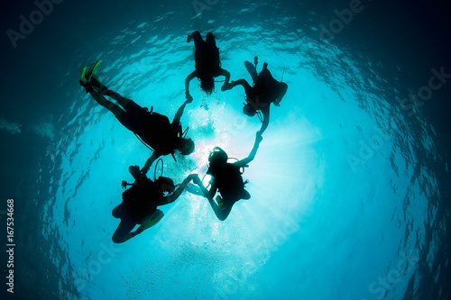 Group of Scuba Divers underwater silhouettes against sun