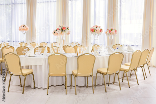 Beautifully decorated room in pastel shades of white with covered tables with flowers in the restaurant for the celebration of the wedding.