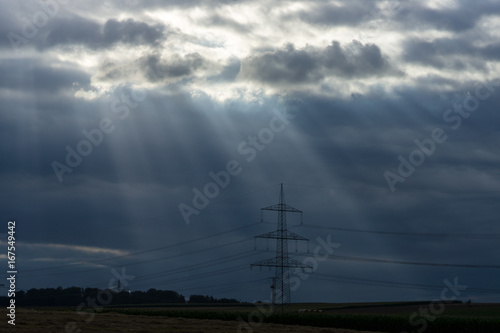 Rays of light making their way through dense clouds. Evening landscape. Agricultural land and power transmission lines.