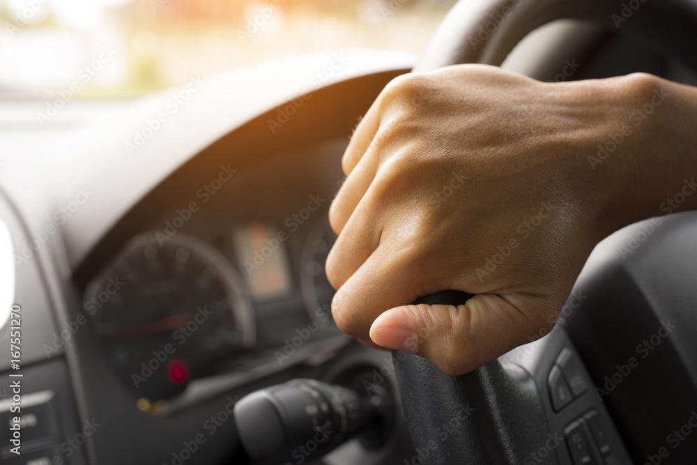 Driver's hands on the steering wheel inside of a car with beautiful green forest perspective, road trip travel concepts.