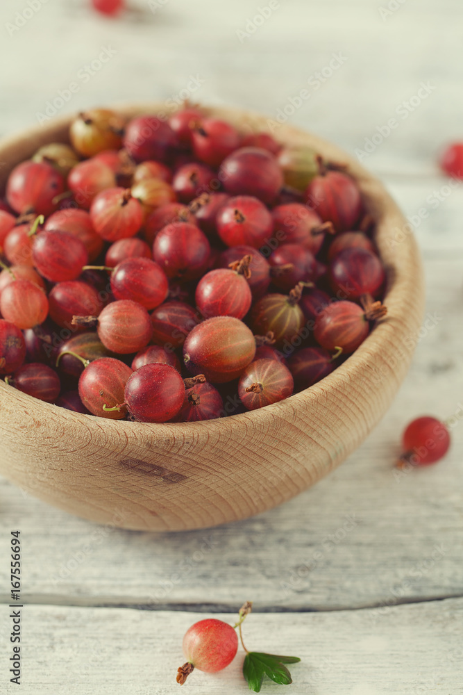 Obraz premium Red gooseberry in a bowl on wooden surface