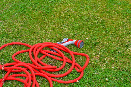 Garden hose bundle on the mown lawn in the summer garden. Reel of hose pipe and spraying head on grass.