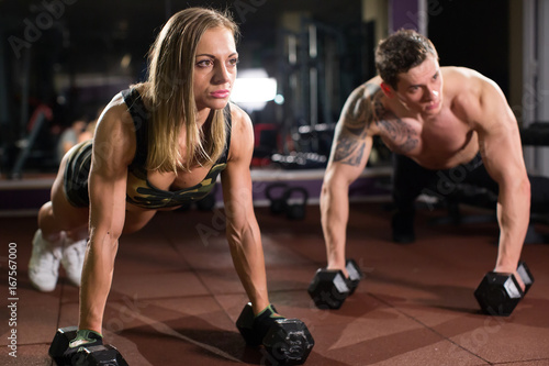 Fototapeta Naklejka Na Ścianę i Meble -  Gym man and woman push-up strength pushup with dumbbell in a fitness workout