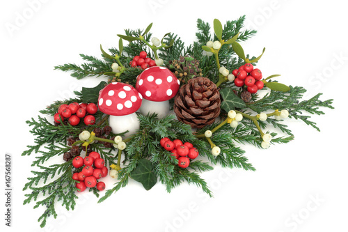 Christmas decoration with fly agaric mushroom ornaments, holly, ivy, mistletoe, cedar and juniper leaf sprigs and pine cone on white background.